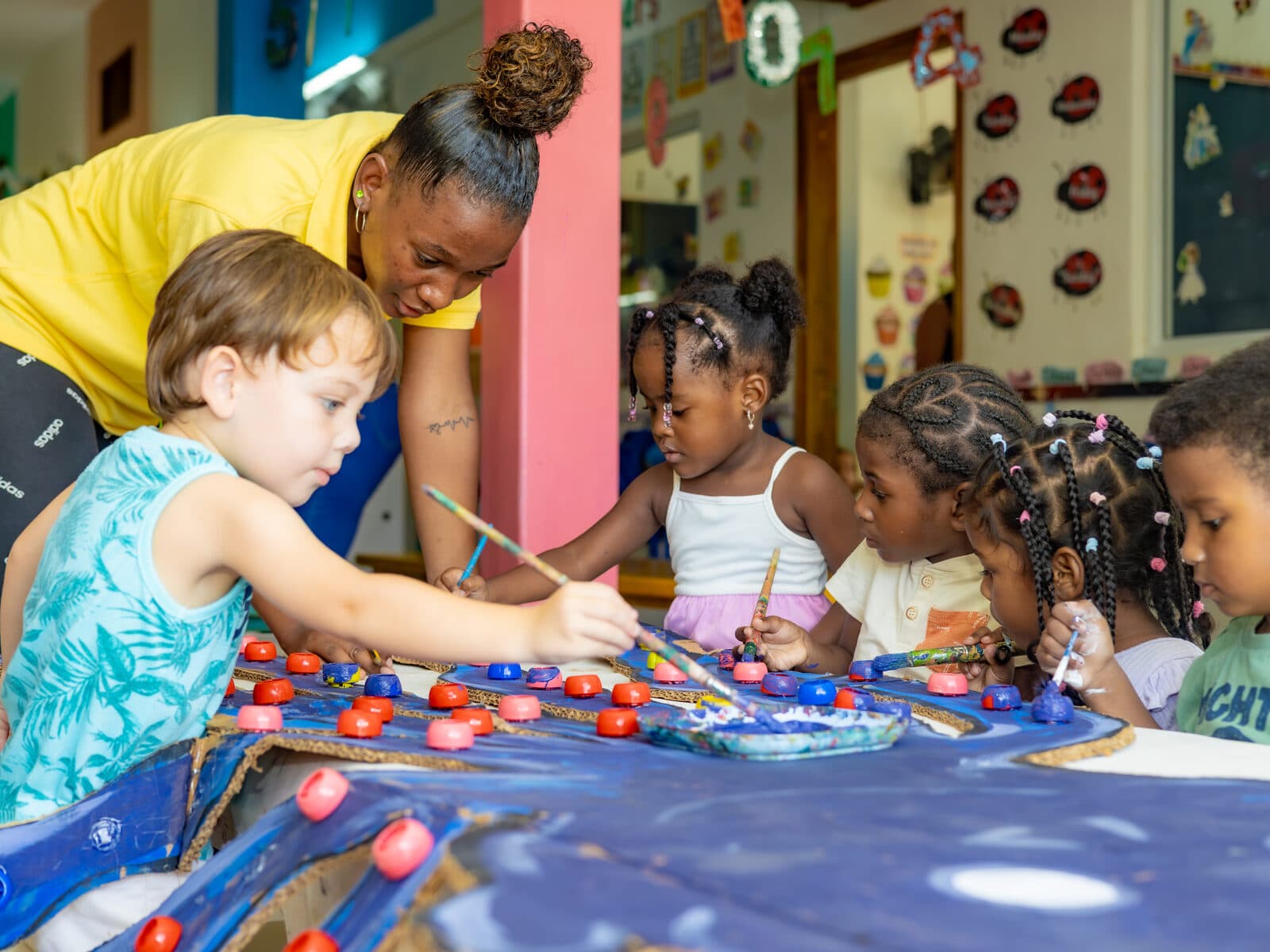 A teacher helping children with a craft activity at a small classroom table