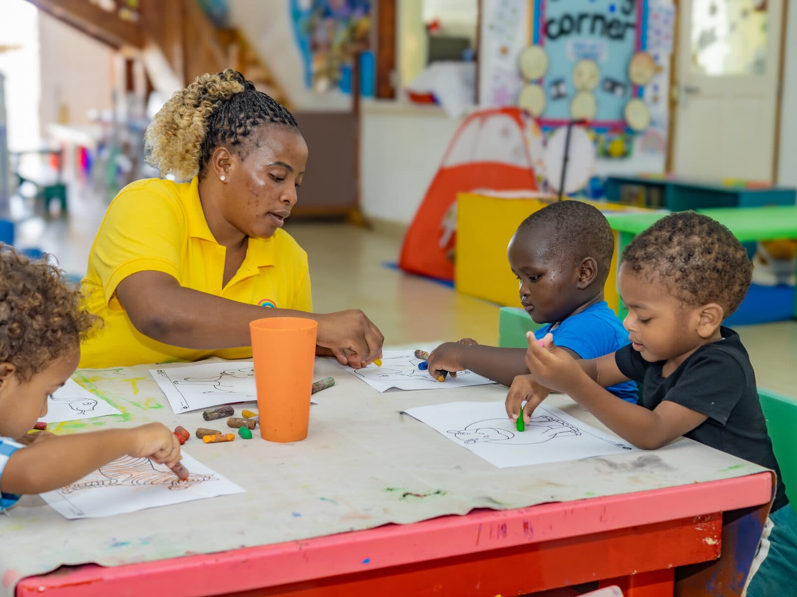 A teacher helping a group of children with a table activity in a colourful classroom