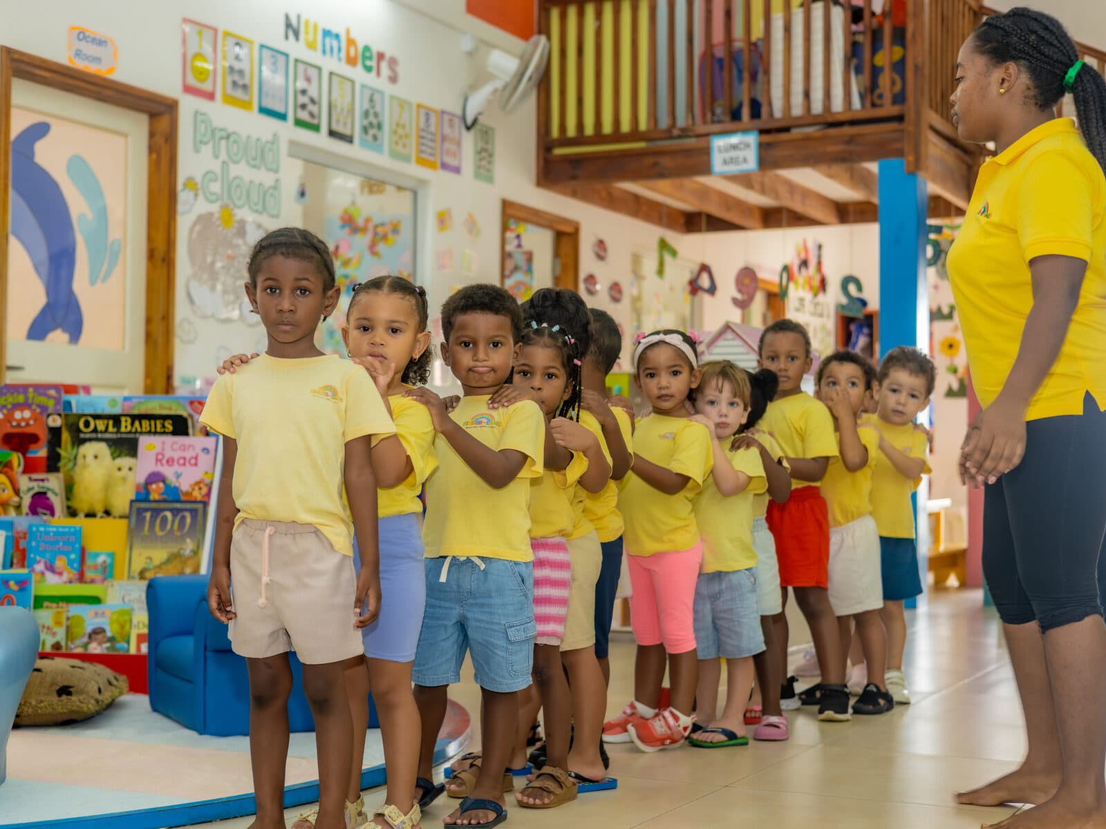 Children lined up together indoors near an alphabet and numbers display