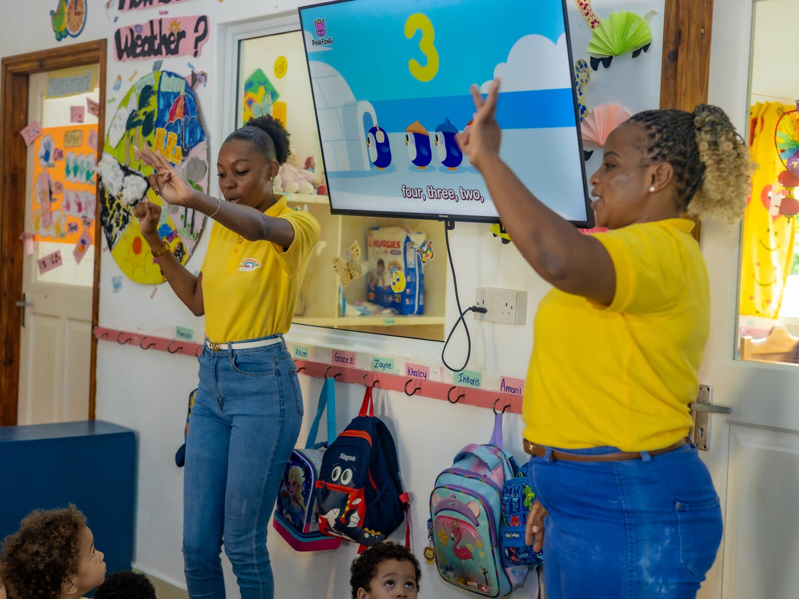 A teacher pointing at a weather and calendar board with children looking on