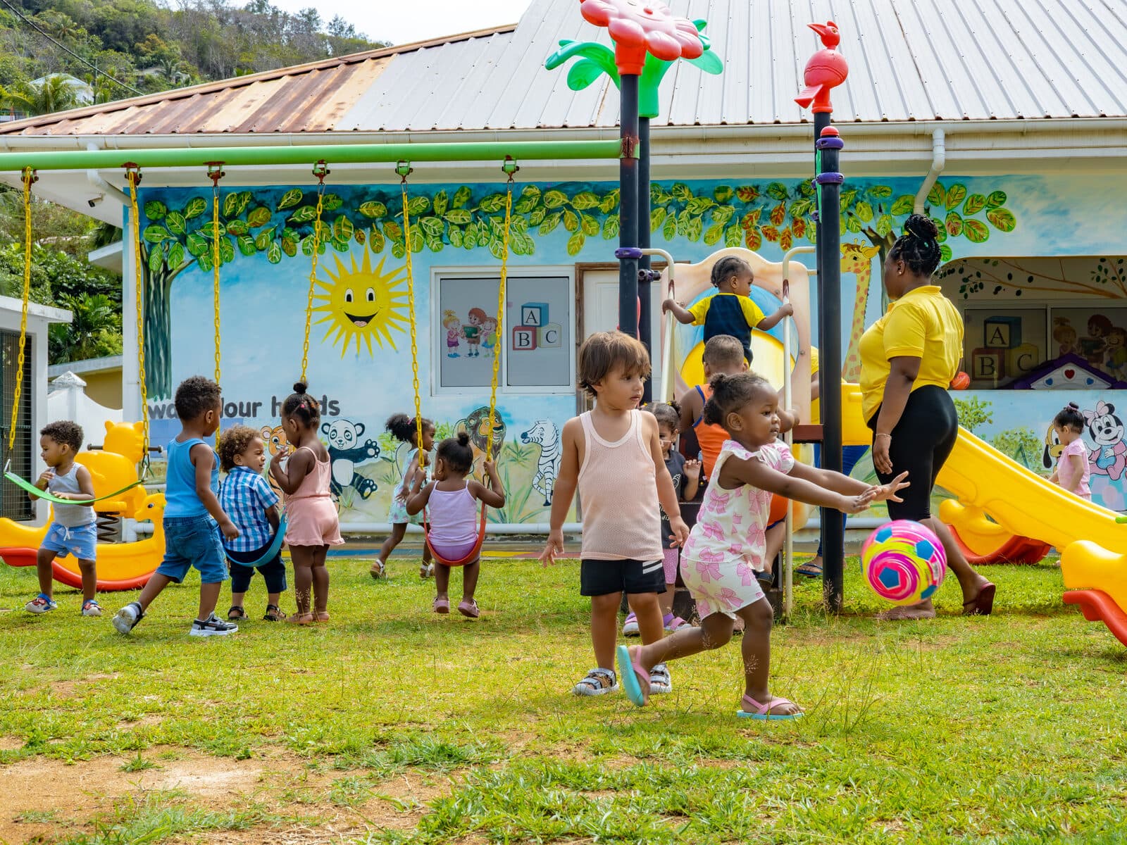 Children playing on the outdoor playground in front of the colourfully painted centre building