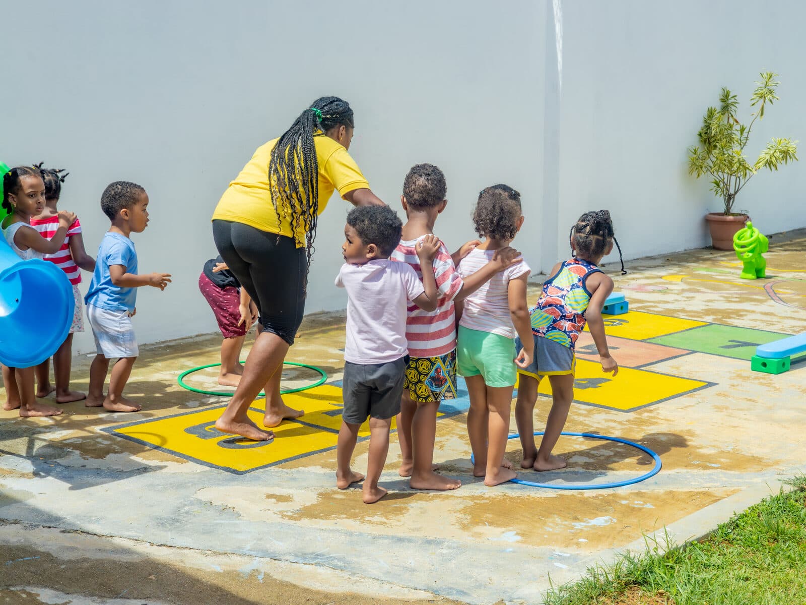 A teacher and children playing together with hula hoops on the outdoor activity mat