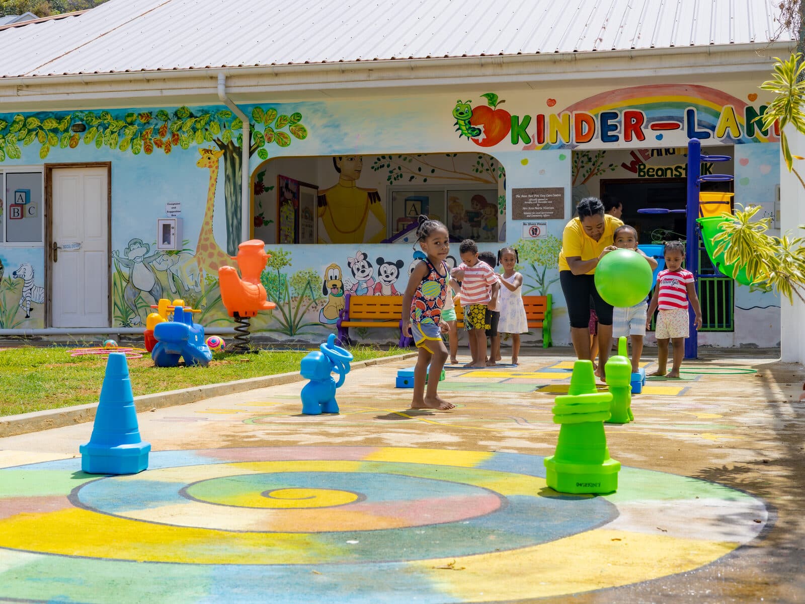 A teacher and children playing with colourful outdoor equipment in front of the centre