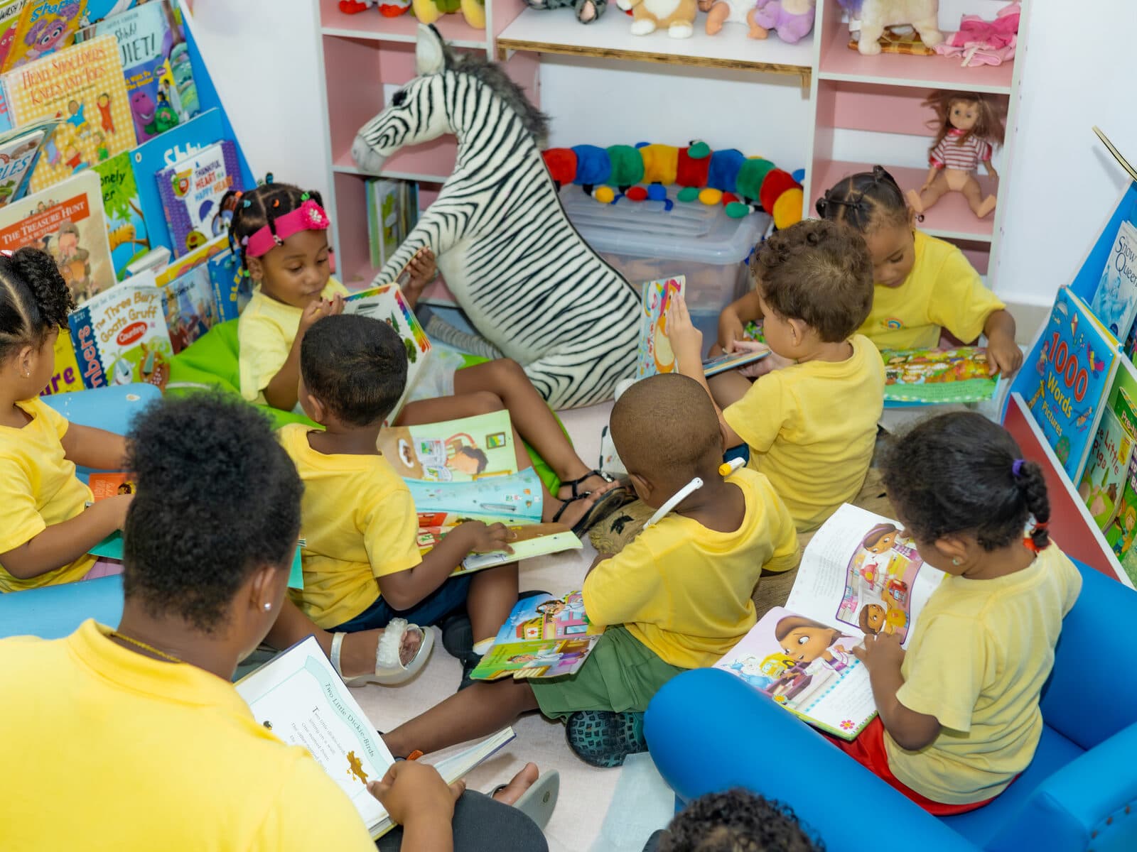 A teacher reading picture books with a group of children in the reading nook