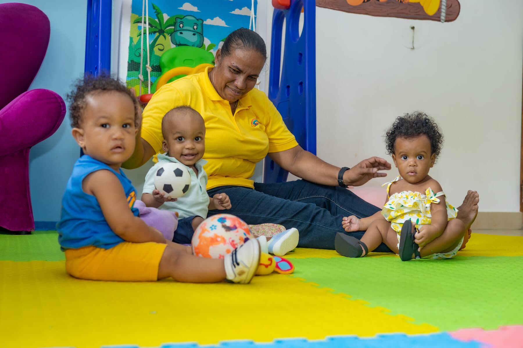 A teacher sitting on a sensory play mat with three infants