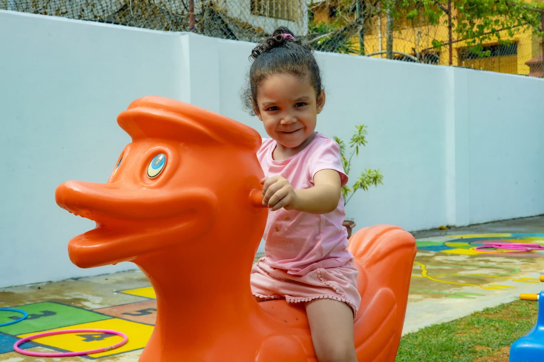 A toddler riding a duck-shaped spring rider in the outdoor play area